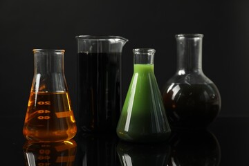 Glass flasks and beaker with different types of oil on black background