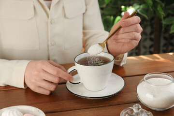 Woman adding sugar into aromatic tea at wooden table indoors, closeup