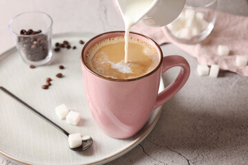 Pouring milk into cup with coffee on light grey textured table, closeup