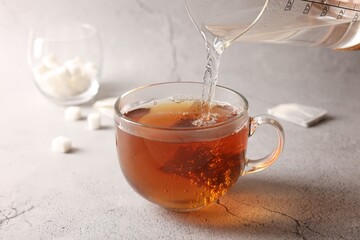 Pouring hot water into cup with tea bag on light grey textured table, closeup