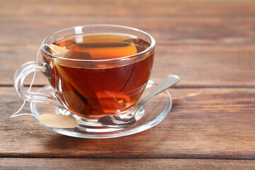 Brewing aromatic tea. Cup with teabag and spoon on wooden table. Space for text