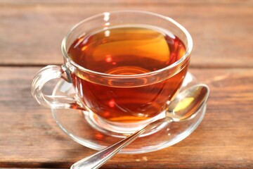 Glass cup of tea and spoon on wooden table