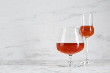 Delicious liqueurs in glasses on white marble table, space for text