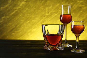 Different delicious liqueurs in glasses on dark wooden table, space for text
