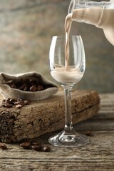 Pouring coffee cream liqueur into glass at wooden table, closeup