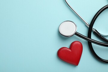 Stethoscope and red heart on light blue background, top view. Space for text