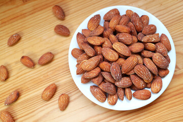 White Plate Full of Almonds with Some Kernels Scattered on Wooden Table