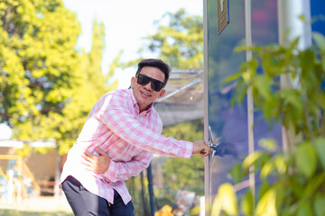 A man in distress desperately tries to open a locked portable toilet in a park setting, reflecting...