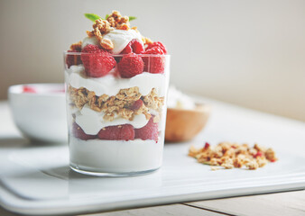 Breakfast, cereal and yogurt with raspberry on plate for vegan food, health and protein in morning. Vitamins, glass and dairy in clear container with fruit for organic nutrition, weight loss and diet