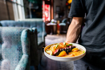 A waiter serves a colorful dish in a cozy restaurant setting, with the focus on the food against a blurred background.