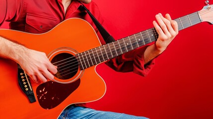 A man in jeans and a red shirt is playing the guitar, red background. Close-up shot
