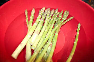 handful of asparagus in a red bowl full of water