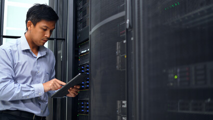 A technician in a blue shirt uses a tablet while inspecting a server rack in a modern data center, ensuring proper functionality.
