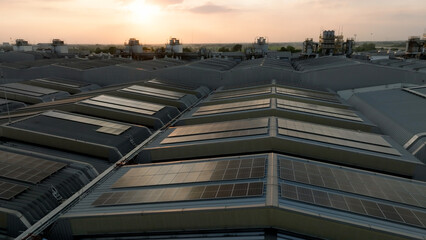 Industrial buildings equipped with solar panels are seen at sunset, highlighting renewable energy...