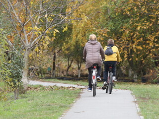 Mom and son ride bicycles along the alley of an autumn park. Healthy and active lifestyle in raising the younger generation. Active recreation in nature. Traveling on two wheels