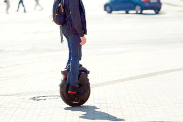 Commuter rides electric monowheel. Man rides an electric unicycle on city street, modern mobility and eco-friendly transportation. View on legs on electric unicycle or mono-wheel on city street © Tricky Shark
