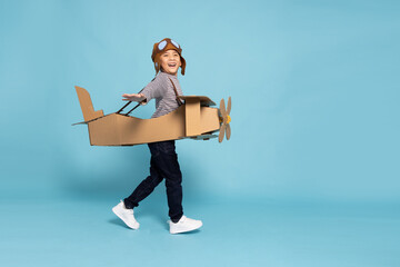 Asian little boy aviator playing and running with cardboard airplane isolated on blue sky...