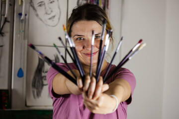 Artistic girl holding many dirty colorful used brushes with both hands.