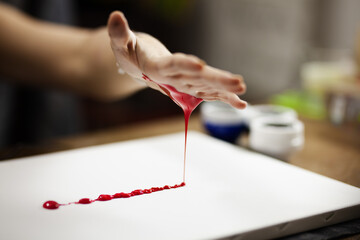 Female artist making an artistic painting with red color on her hand.
