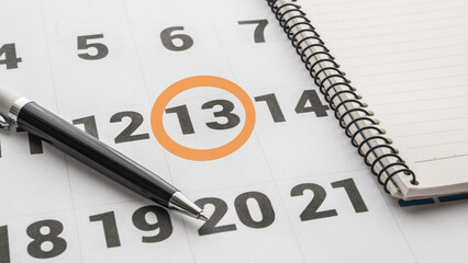 calendar with the 13th marked with a red circle. Notebook, calendar and pen on the table