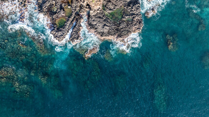 aerial top view of coastline with deep cliffs, blue water and waves hitting the shoreline 