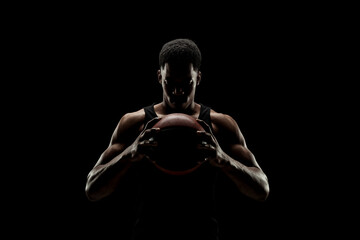 Basketball player holding a ball against black background. Serious concentrated african american man.
