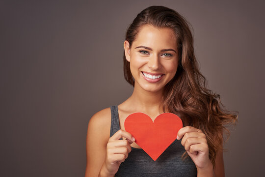 Portrait, happy and woman with paper heart in studio for romance, support and care isolated on background. Face, smile and model with love sign for valentines day, kindness and emoji for social media