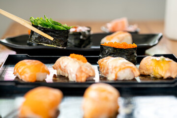 Assorted sushi pieces including seaweed salad gunkan and salmon nigiri on black tray, with chopsticks holding one piece