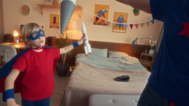Medium shot of cheerful Caucasian boy and his father both dressed in superhero costumes launching handmade rockets at home while playing together at daytime