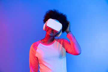 Profile thinking young beautiful African wearing VR glasses metaverse isolated on blue and pink...