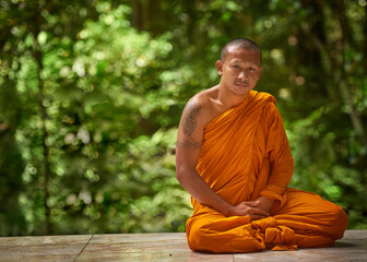 Calm, man and buddhist monk in portrait on bench for peace, zen and outdoor meditation at shrine. Male person or missionary and prayer pose with orange robe for spirituality, worship and wellness