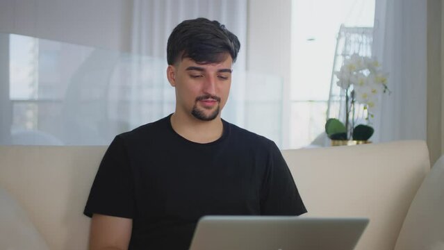 Smiling focused millennial guy typing on computer surfing web looking at screen. Young man using laptop to chat online. Studying online working from home in internet. Having fun using a computer.