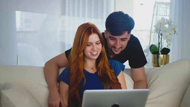 A young couple online shopping together. Married couple smiling and looking at a laptop, planning a trip or shopping for home items, representing shared moments and digital lifestyle.