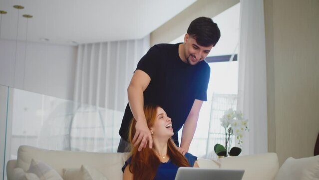 A young couple enjoying quality time together. Boyfriend massages his girlfriend's shoulders while they look at something on the laptop, representing love and relaxation.