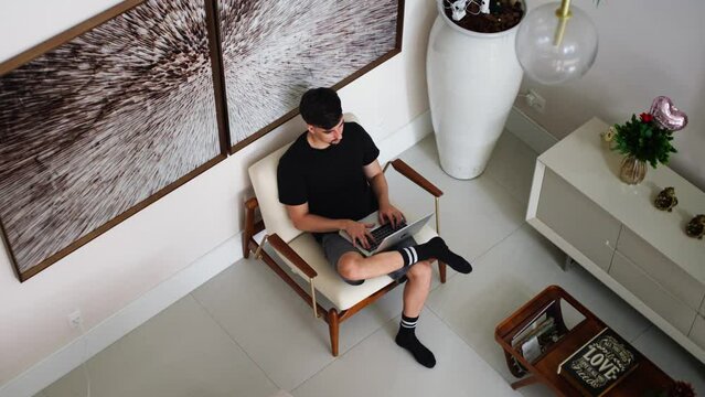 Man Working on a Laptop at Home. Top View of a Guy Sitting in a Chair and Using Laptop in a Modern Home Environment. Student studying online through laptop at home