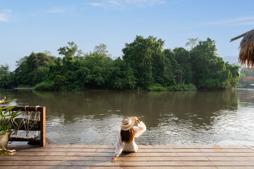 girl or woman sitting and relaxing bench by the river On the balcony made of wood. River Kwai in the jungle, Thailand, resting place, resort