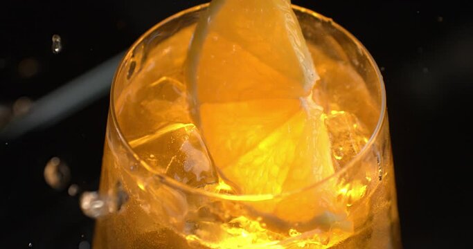 Super slow motion macro of bartender puts slice of fresh orange while preparing alcoholic cocktail in transparent glass for customer in bar or disco club at 1000 fps.