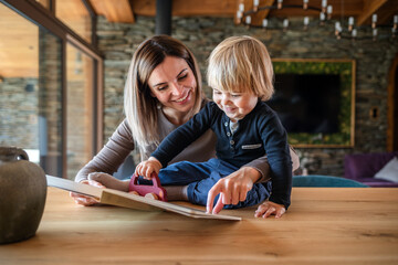 Mother and son spending time together at home reading a childrens book at dining table