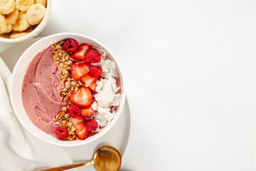 Strawberry smoothie bowl topped with berries, granola and coconut chips, overhead view with copy space