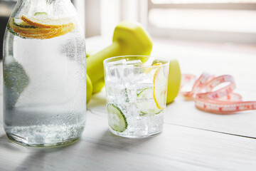 Glass, dumbbell and fitness with lemon water on table for nutrition, detox and healthy drink in...
