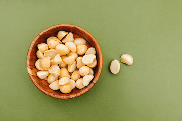 Macadamia nuts in a small wooden bowl on green background, top view