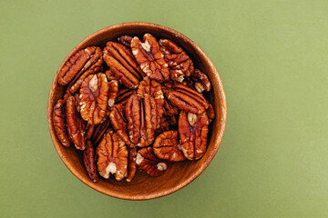 Pecan nuts in a small wooden bowl on green background, top view