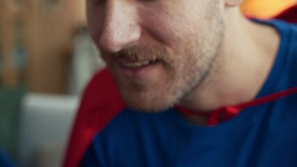Tilt up closeup of Caucasian man with son dressed like superheroes playing video games together with joysticks, sitting on couch in living room at daytime