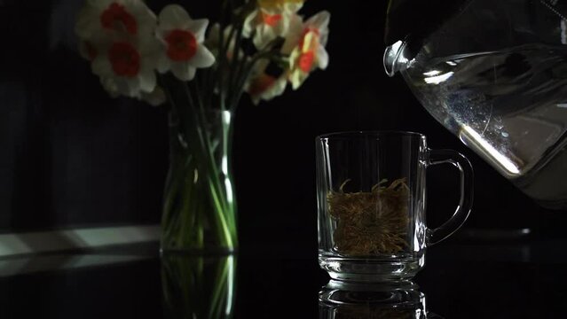 Pouring boiling water into a transparent mug with a flower. Dark scene. 60fps Slow motion