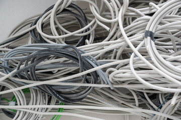 cable spaghetti. tangled mass of various white, gray, and black cables coiled and intertwined with...