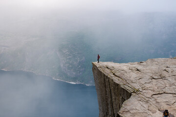 Preikestolen, Norway, A lone hiker stands on the precipice of a dramatic cliff in Norway, with a...