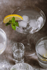 Collection of various glasses on silver tray filled with clear cold drinks with ice, lemon and mint on grunge wall background. Cocktail party