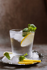 Glass of refreshing sparkling water with ice, lemon and mint on silver tray