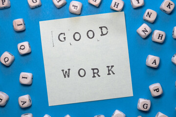 good work stamped on white sticky note on a bright blue background with cubes with letter around it