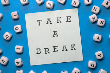 take a break stamped on white sticky note on a bright blue background with cubes with letter around...